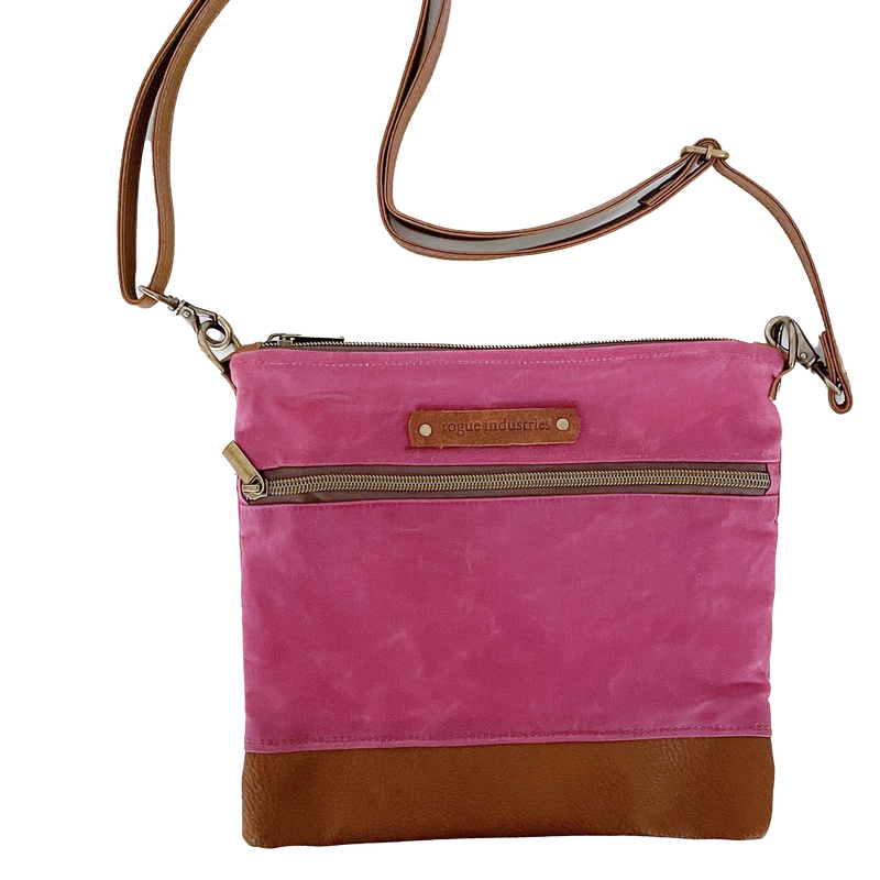 A pink and waxed canvas Ellis River Crossbody Bag by Rogue Industries on a white surface.