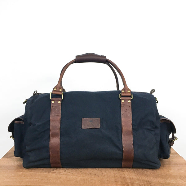 A blue, water-resistant White Cap waxed canvas duffle bag with brown straps by Rogue Industries.
