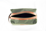 A green Waxed Canvas Dopp Kit by Rogue Industries with a brown leather zipper partially open, viewed from above. Made in the USA.