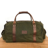 A Rogue Industries White Cap Waxed Canvas Duffle with full-grain leather straps and handles is placed on a wooden surface against a plain white background.
