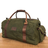 A White Cap Waxed Canvas Duffle from Rogue Industries, crafted from water-resistant waxed canvas and featuring brown full-grain leather straps, two handles, and a shoulder strap, placed on a wooden surface.