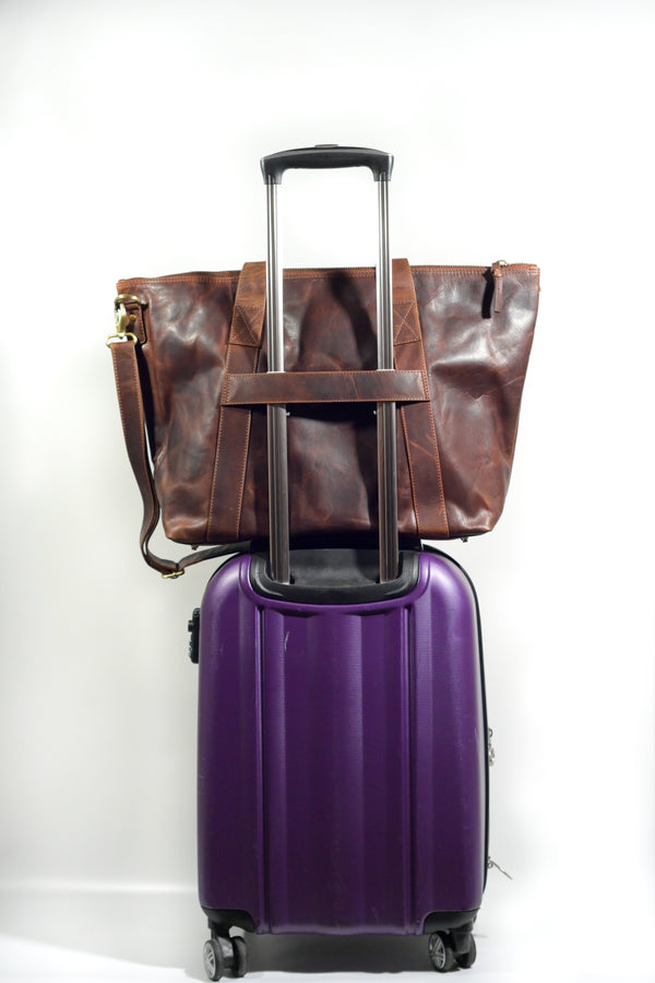 A purple suitcase with a luggage strap on top of a brown Rogue Industries Rockport Leather Weekend Tote.