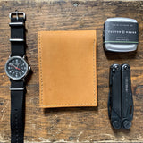 A Heritage Wallet in Baseball Glove Leather made by Rogue Industries, watch, and other items on a wooden table.