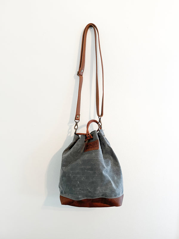 A small grey Rogue Industries Kennebunkport bucket bag hanging on a wall.