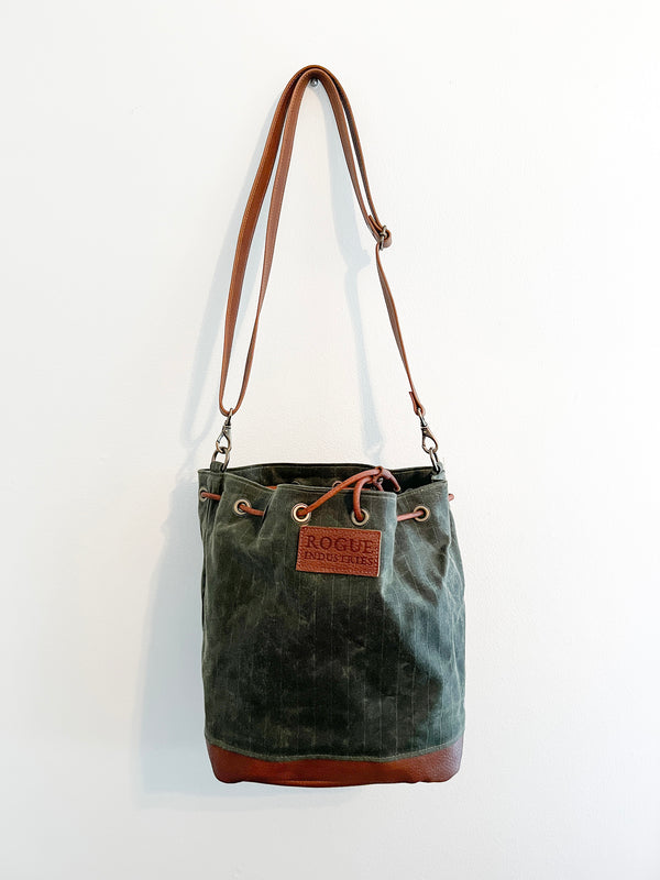 A green Rogue Industries Kennebunkport Bucket Bag hanging on a wall.