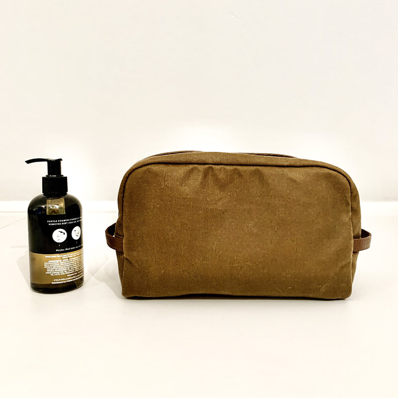 A durable tan Rogue Industries waxed canvas Dopp kit made in the USA with a bottle of soap next to it.