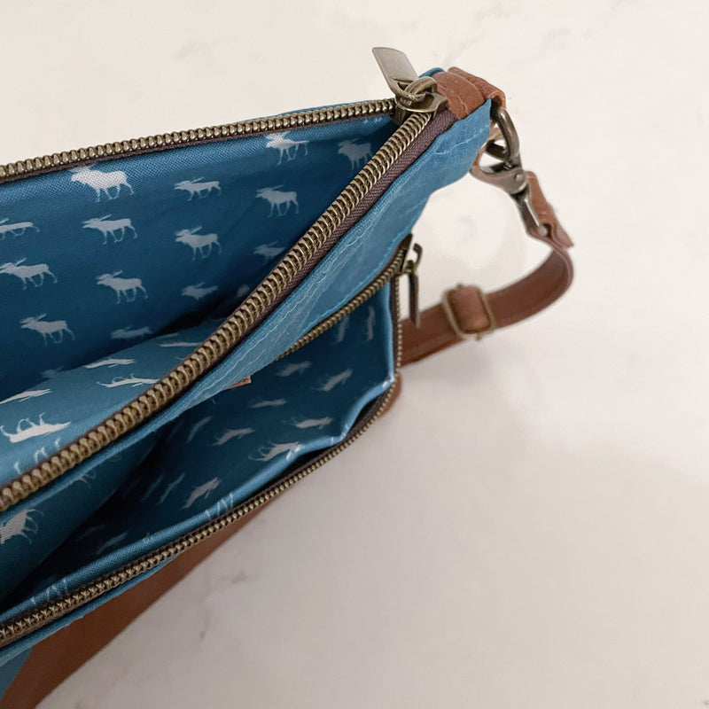 A blue Ellis River crossbody bag with a deer print on it by Rogue Industries.