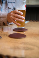 A person drinking a beer on Sebago Camp Coasters atop a wooden table.