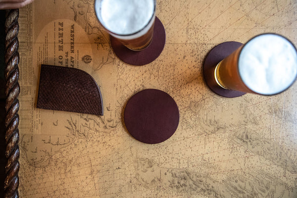 Two glasses of beer on Sebago Camp Coasters rest on a table next to a map.