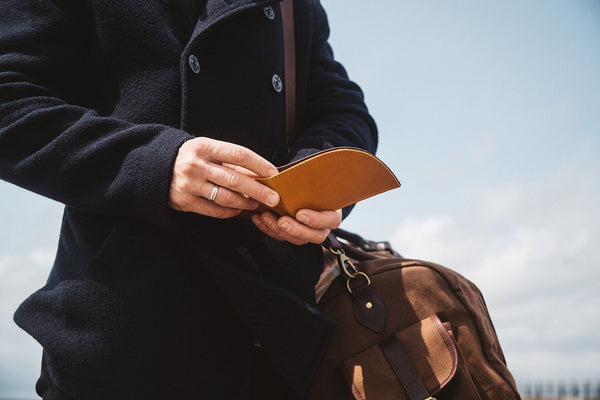 A man is holding a brown leather RFID-blocking Rogue Front Pocket Wallet in Ballglove from Rogue Industries.