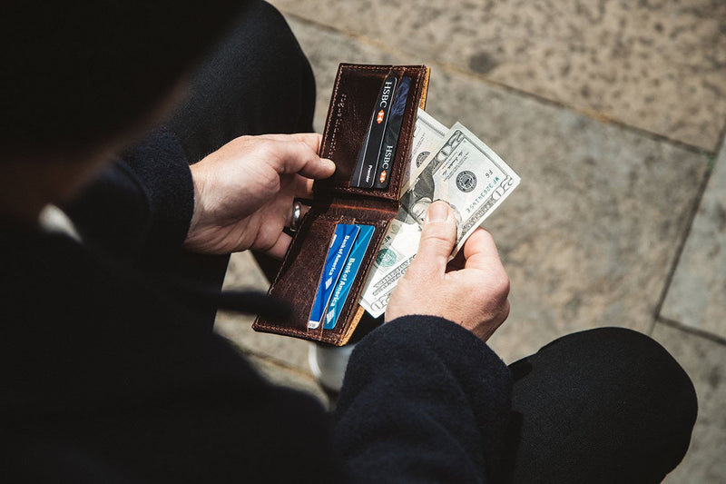 A man holding a Heritage Wallet from Rogue Industries made of genuine cowhide leather with money in it.