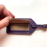A person is holding a purple Rogue Industries cowhide leather luggage tag.