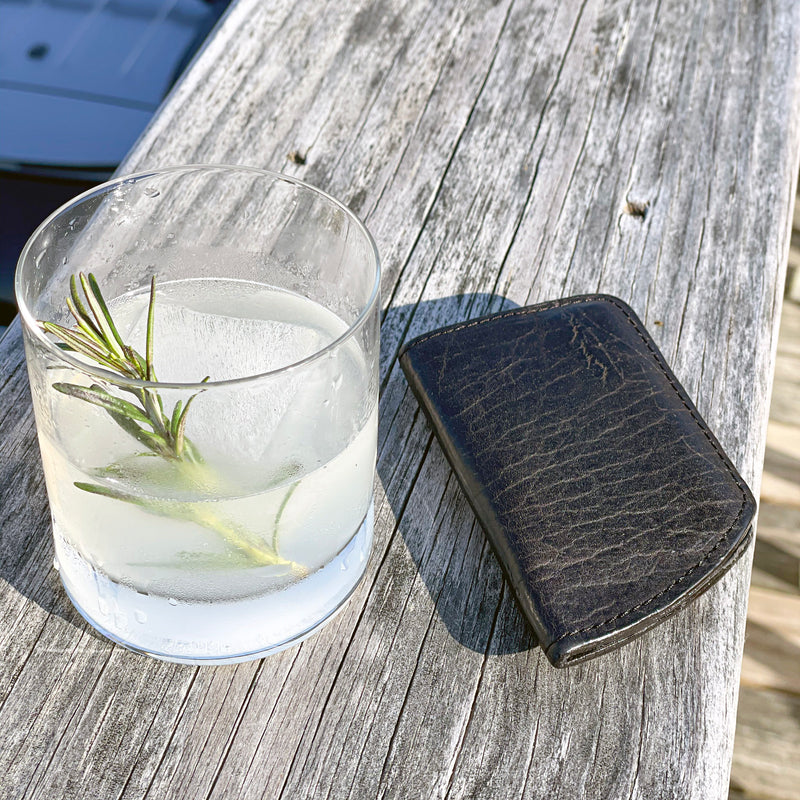 A Rogue Industries Minimalist Wallet and a drink on a wood surface.