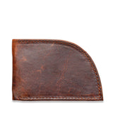 A weathered brown leather slim wallet, the Factory Second PREVIOUSLY EMBOSSED Made in Maine Front Pocket Wallet by Rogue Industries, features a curved bottom right corner and shows signs of wear and aging. The visible stitching around the edges adds to its rustic charm. This RFID-blocking wallet, crafted in Maine, is closed and appears empty.