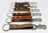 A row of different colored durable Rogue Industries leather keychains on a white surface.