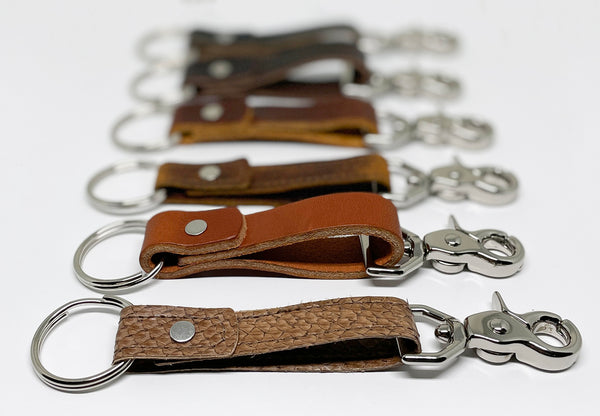 A row of different colored durable Rogue Industries leather keychains on a white surface.