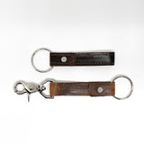 Two Rogue Industries brown leather keychains with a nickel rivet on a white background.