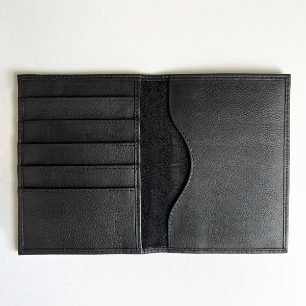 A monogrammed Rogue Industries black leather passport holder on a white surface.