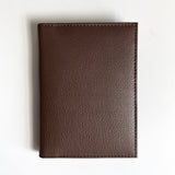 A Rogue Industries brown leather passport holder with monogramming on a white surface, perfect for travelers.