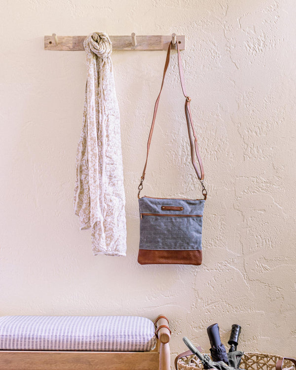A bench with a bottle of wine and an Ellis River Crossbody Bag by Rogue Industries hanging on the wall.