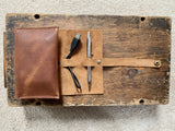 A pen case and pencils on a wood surface, next to a top-grain leather Rogue Industries Leather Tech Organizer.
