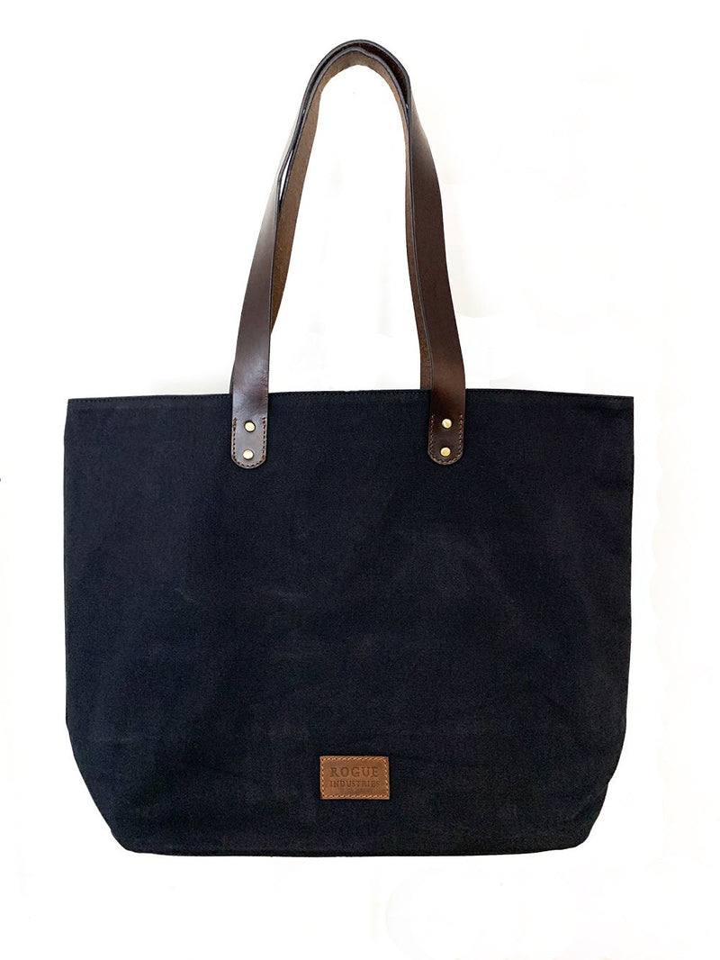 A durable, black Rogue Industries waxed canvas tote bag with top-grain leather straps.