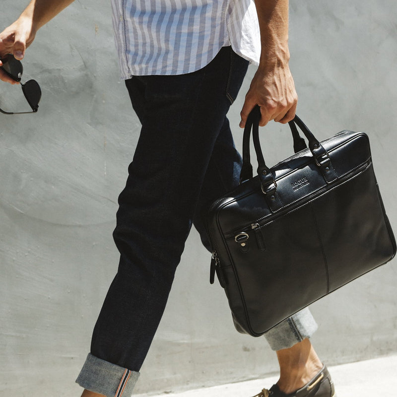 A man carrying a black West End Slim Leather Laptop Bag by Rogue Industries.