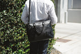 A person carrying a black West End Slim Leather Laptop Bag from Rogue Industries.