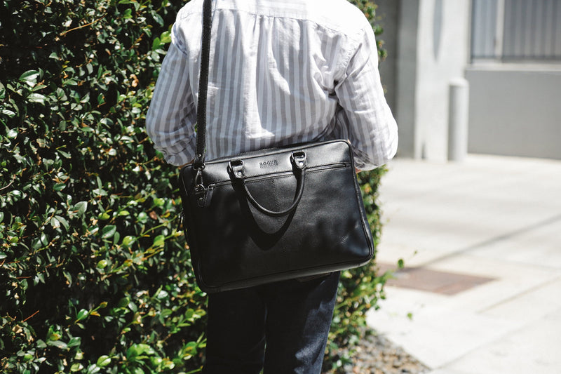 A person carrying a black West End Slim Leather Laptop Bag from Rogue Industries.