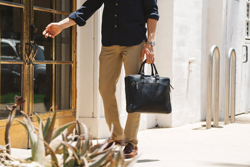 A man in a tan shirt holding a Rogue Industries West End Slim Leather Laptop Bag.
