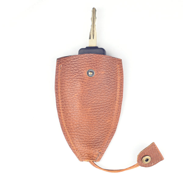A single key in a brown textured leather key holder with a button clasp lies on a white background. This durable Rogue Industries Rogue Leather Key Protective Case ensures your keys are stylishly secured and easily accessible.