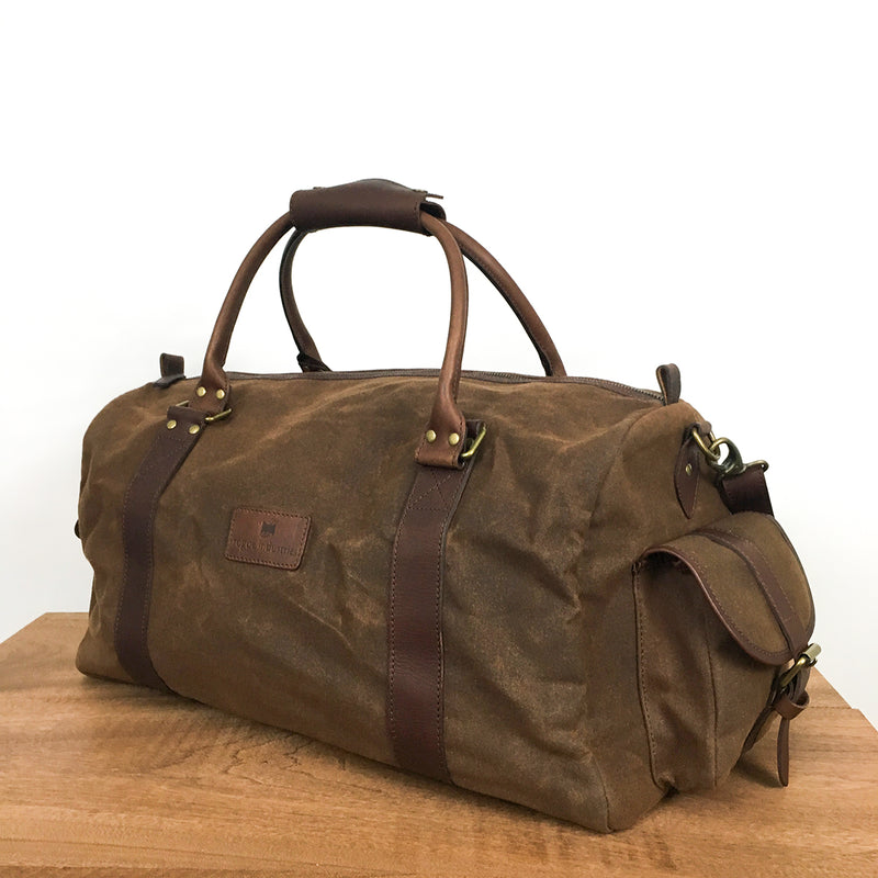 A brown White Cap waxed canvas duffle bag by Rogue Industries on a wooden table.