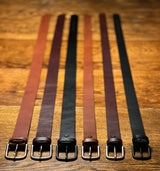 Five Chamberlain Leather Belts - 1.25" Wide by Rogue Industries are lined up on a wooden table.