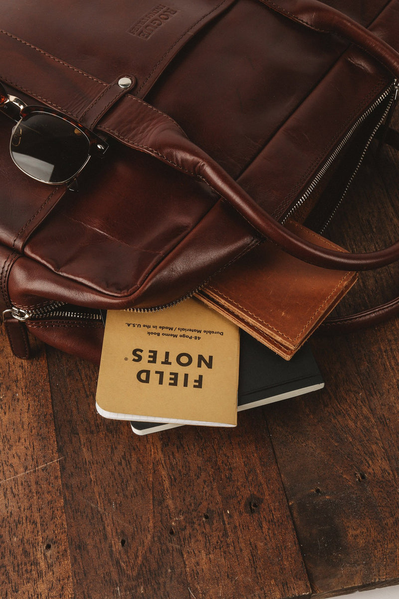 A Katahdin leather briefcase by Rogue Industries sitting on top of a wooden table.