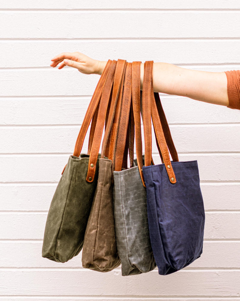 A woman is holding four durable Rogue Industries Allagash River Tote Bags in front of a white wall.